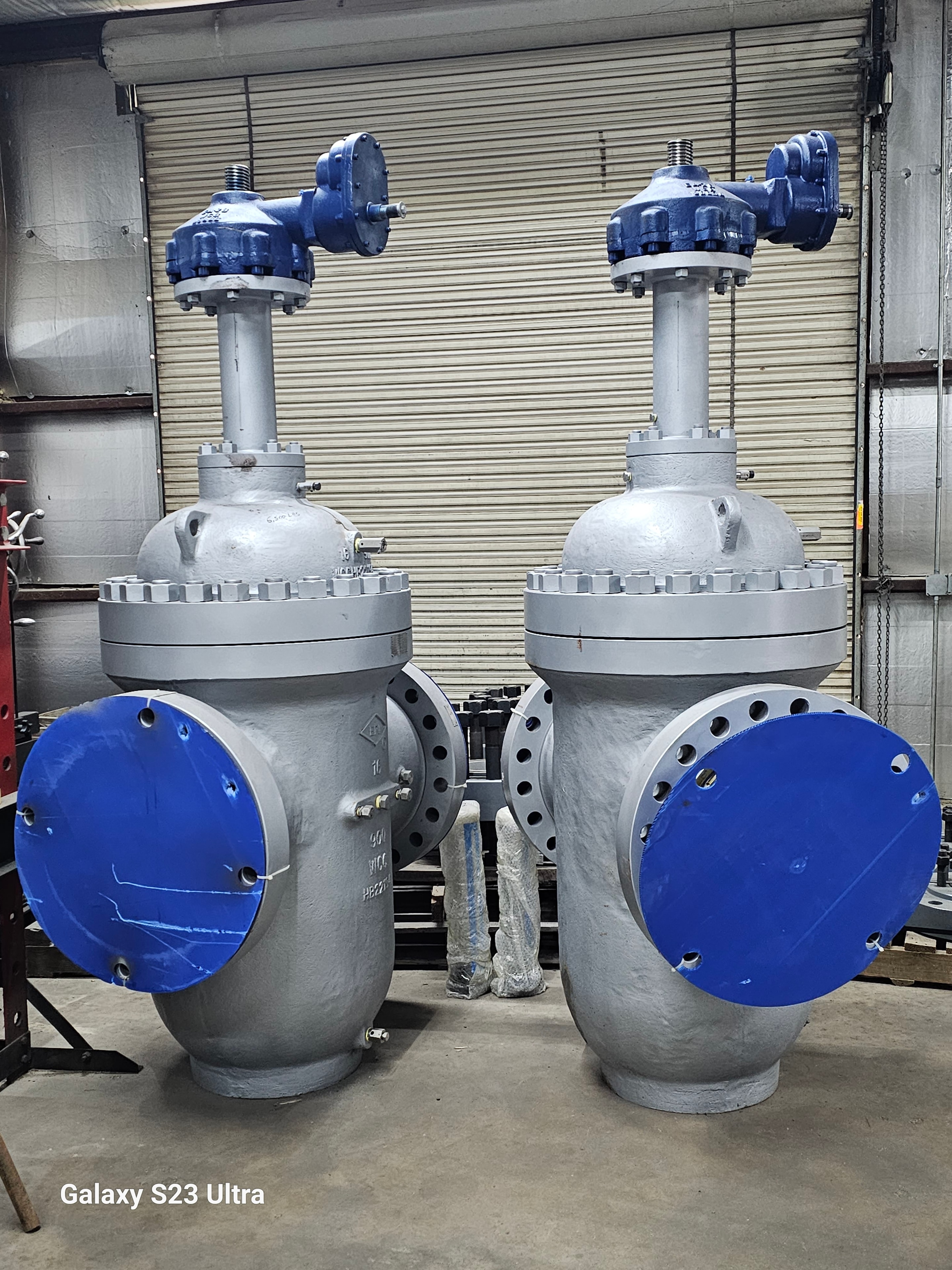 Two large gray industrial valves with blue flange covers in a warehouse